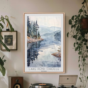 May include: A framed watercolor print of Lake Pend Oreille in Idaho. The artwork depicts a serene lake scene with mountains in the background, trees along the shoreline, and the lake's reflection. The print is in a wooden frame and includes the lake's name and state.