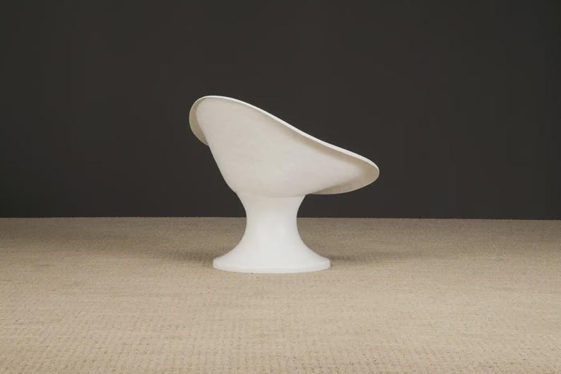 May include: A white, modern-style chair with a curved seat and a pedestal base. The chair is made of a smooth, glossy material and is set against a dark gray background. The chair's design is minimalist and sculptural.