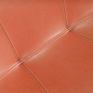 Pu&ograve; includere: Primo piano di pelle marrone-arancio cucita con filo scuro. La pelle &egrave; divisa in forme geometriche dalle cuciture, creando una superficie strutturata. Le cuciture sono visibili e aggiungono dettagli.