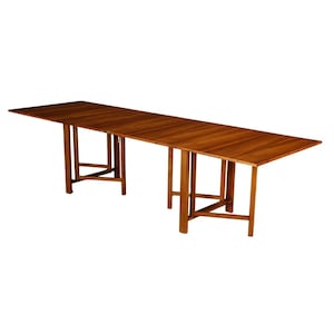 May include: A long, rectangular wooden table with a warm brown finish. The table has a series of legs that are connected by horizontal supports. The table is ideal for dining or as a workspace. The table is approximately 120 inches long.