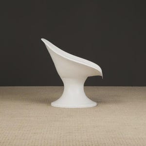 May include: A white, modern-style chair with a curved back and a pedestal base. The chair has a smooth, glossy finish and is set against a dark gray background. The chair's design is minimalist and sculptural.