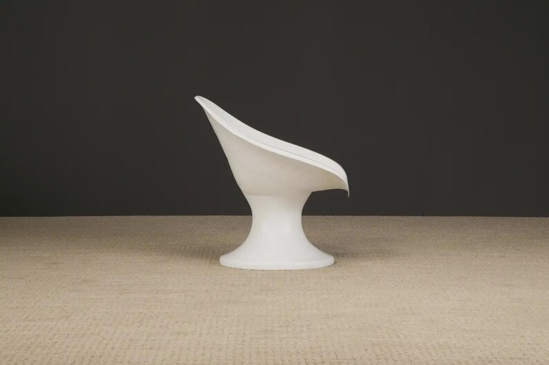 May include: A white, modern-style chair with a curved back and a pedestal base. The chair has a smooth, glossy finish and is set against a dark gray background. The chair's design is minimalist and sculptural.