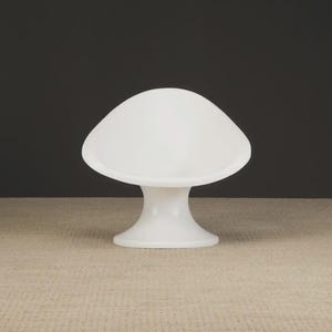 May include: A white, mushroom-shaped lamp with a rounded top and a flared base. The lamp is made of a smooth, opaque material and sits on a neutral-toned surface against a dark background. The lamp's height is approximately 10 inches.