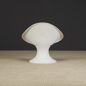 May include: A white, abstract, sculptural object with a flared top and a pedestal base. The object has a smooth, matte finish and is set against a dark background. The shape resembles a stylized shell or a mushroom.