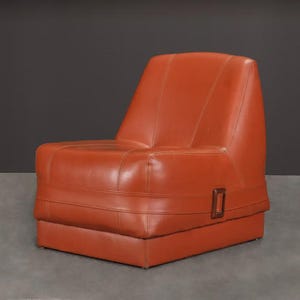 Pu&ograve; includere: Poltrona in pelle arancione con schienale alto e base rettangolare. La sedia ha una forma squadrata con cuciture a vista e un piccolo accento in legno rettangolare sul lato. Stile moderno della met&agrave; del secolo.