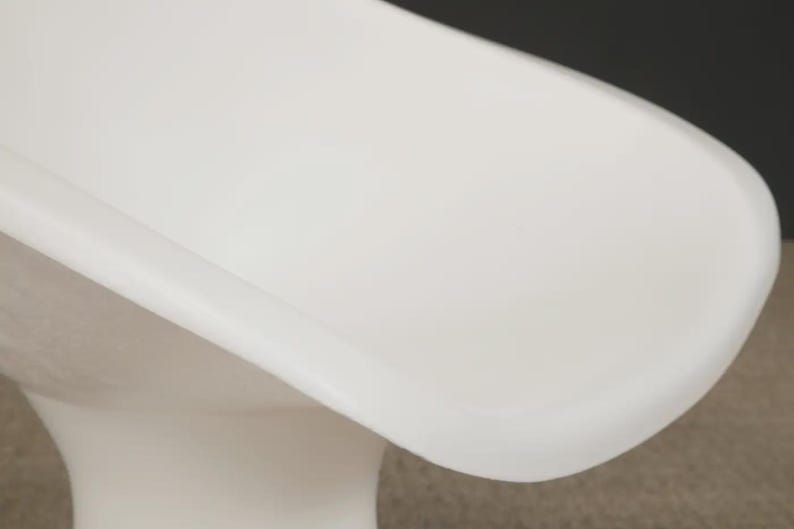 May include: A modern, white, molded plastic chair with a curved seat and a pedestal base. The chair has a smooth, glossy finish and a minimalist design, suitable for various interior styles.
