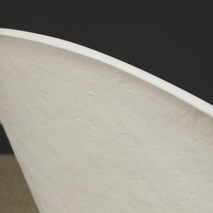 May include: Close-up of a white, curved object with a textured surface. The object has a rounded edge and a smooth, clean line. The background is a dark gray color.