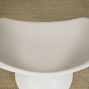 May include: A white, modern-style chair with a curved seat and a pedestal base. The chair has a smooth, matte finish and a minimalist design. The chair is likely made of plastic or a similar material.