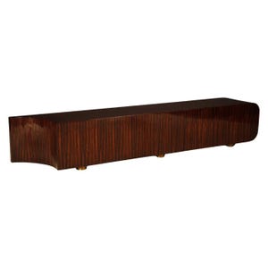 May include: A long, rectangular, wooden cabinet with a high-gloss finish. The cabinet is a dark reddish-brown color with vertical wood grain. It has a curved end and sits on three small, gold-colored feet.