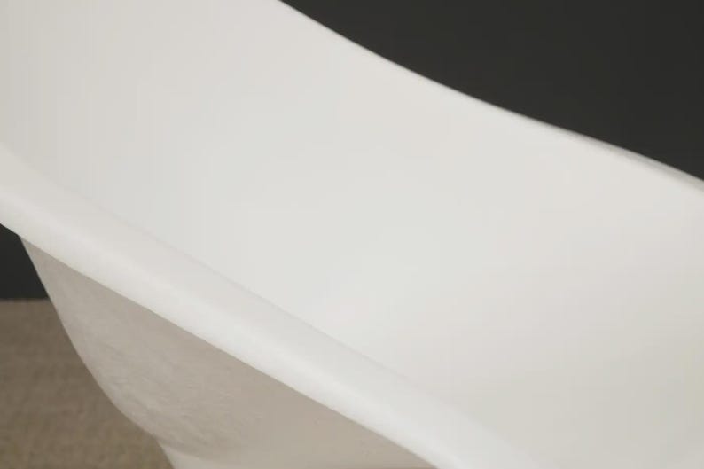 May include: A white, modern bathtub with a curved design. The tub has a smooth, glossy finish and a minimalist aesthetic. The image shows a close-up of the tub's interior and exterior.