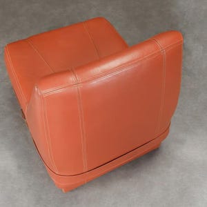 Pu&ograve; includere: Una poltrona in pelle arancione con schienale basso e braccioli. La sedia presenta dettagli cuciti e una base arrotondata. Il colore &egrave; un arancione rossastro caldo e la sedia sembra essere in buone condizioni.