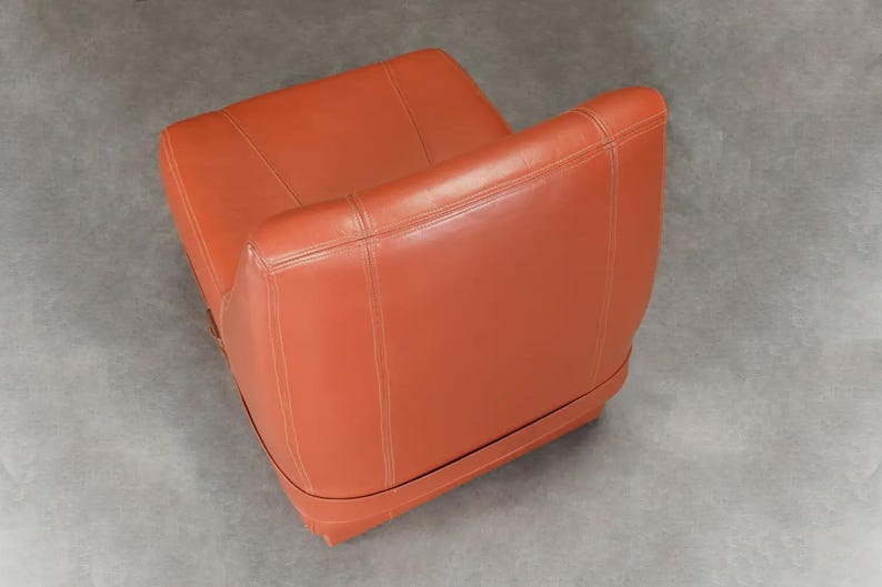 Pu&ograve; includere: Una poltrona in pelle arancione con schienale basso e braccioli. La sedia presenta dettagli cuciti e una base arrotondata. Il colore &egrave; un arancione rossastro caldo e la sedia sembra essere in buone condizioni.