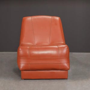 Pu&ograve; includere: Una sedia in stile retr&ograve; in una calda tonalit&agrave; rosso-arancio. La sedia ha uno schienale alto e una base rettangolare. La seduta e lo schienale sono imbottiti con cuciture orizzontali. Realizzata in un materiale liscio simile alla pelle.