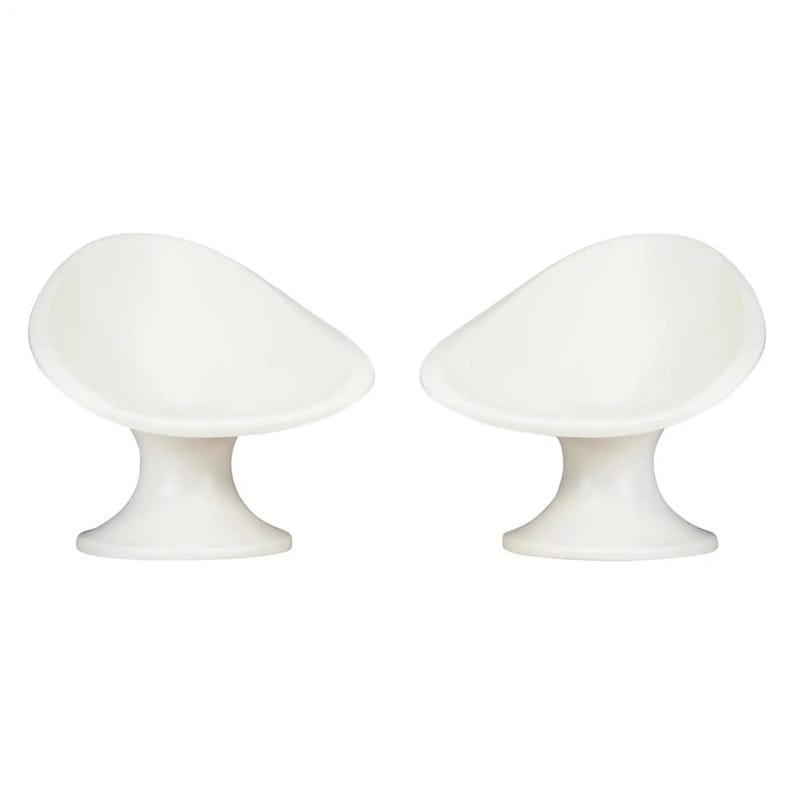 May include: Two white, modern-style chairs. Each chair has a rounded seat and a pedestal base. The chairs are made of a smooth, glossy material and are set against a white background. The design is minimalist.