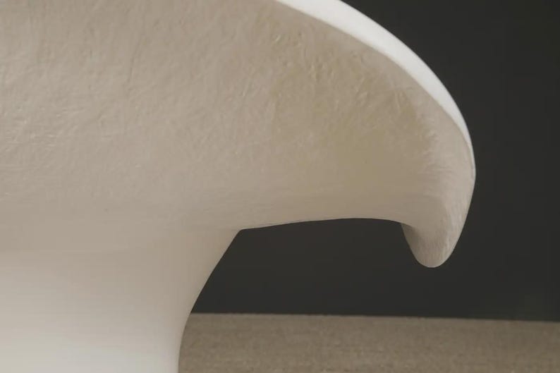 May include: A close-up of a white, curved object with a textured surface. The object has a smooth, rounded edge and a slight overhang, set against a dark background. The shape suggests a sculptural or decorative element.