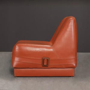 Pu&ograve; includere: Una poltrona in stile retr&ograve; in pelle marrone rossiccio. La poltrona ha uno schienale alto e una seduta bassa, con una base rettangolare. Un dettaglio con fibbia marrone scuro &egrave; visibile sul davanti. La poltrona &egrave; alta circa 76 cm.