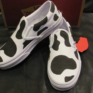 May include: A white ceramic mug with a black handle and the text "But First, Coffee" in a black, bold font. The mug is on a white surface. The mug is approximately 10 cm tall.