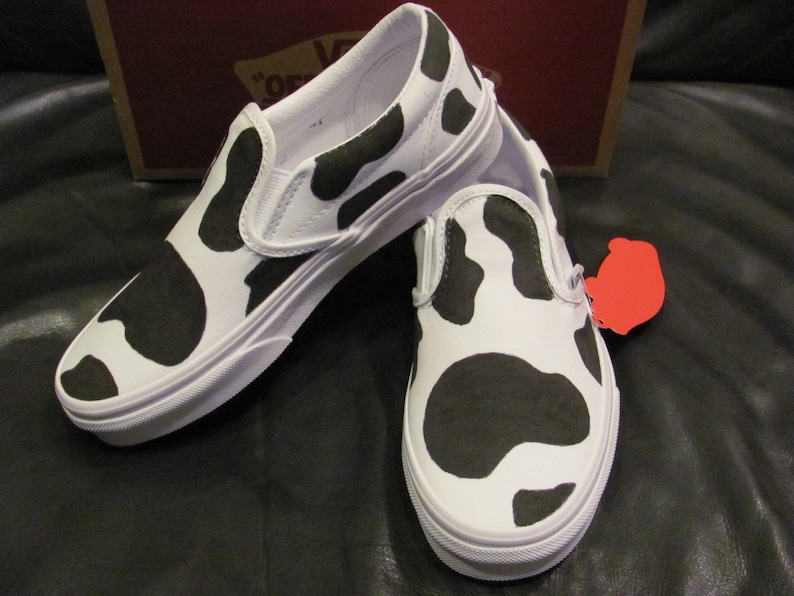 May include: A white ceramic mug with a black handle and the text "But First, Coffee" in a black, bold font. The mug is on a white surface. The mug is approximately 10 cm tall.