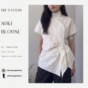 May include: Cream-colored short-sleeve blouse with blue vertical stripes. The blouse features a mandarin collar, asymmetrical button closure, and a draped, knotted design at the waist. The text "SUKI BLOUSE" is visible.