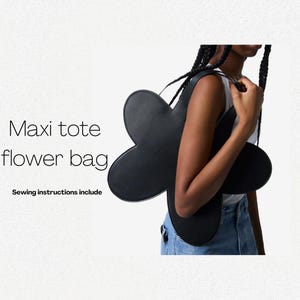 Op de afbeelding: Een zwarte, bloemvormige tote bag met een groot, afgerond silhouet. De tas wordt door een persoon gedragen, en de band is zichtbaar.