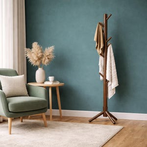 May include: A dark brown wooden coat rack with multiple branches for hanging items. Two towels are draped over the branches. The rack stands on a wooden floor in front of a teal wall. A green armchair, side table, and rug are also in the room.
