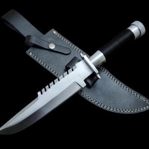 May include: A silver and black hunting knife with a serrated blade and a leather sheath.