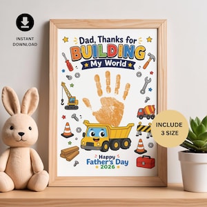 May include: A framed print with the text "Dad, Thanks for BUILDING My World" and "Happy Father's Day 2026." The print features a handprint, construction vehicles, and tools. The frame is light brown.