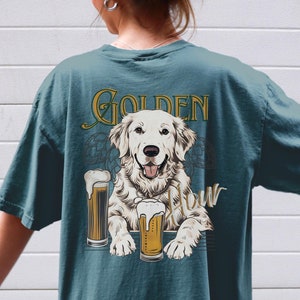 May include: A teal blue t-shirt with a graphic of a golden retriever dog holding two glasses of beer. The text "Golden Hour" is printed above the dog.
