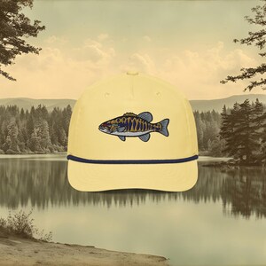 A banana yellow baseball cap with a blue rope and a blue, ochre, and white embroidered smallmouth bass fish on the front.