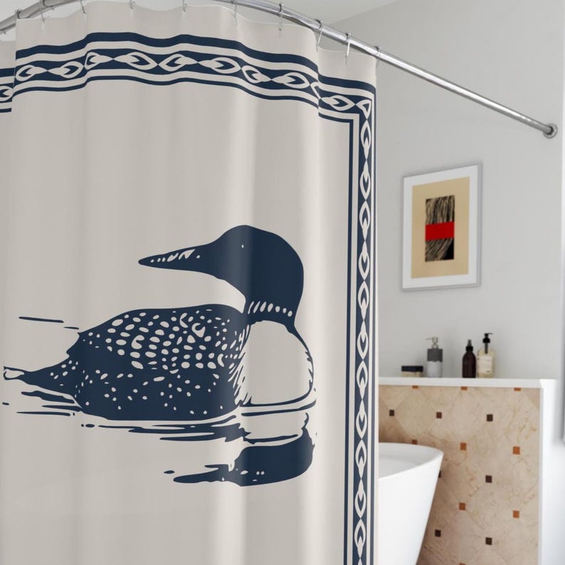 A white shower curtain featuring a navy blue illustration of a loon swimming on water. The loon is detailed with white spots and a black head. The curtain has a navy blue border with a decorative pattern, and is hanging in a rustic bathroom.