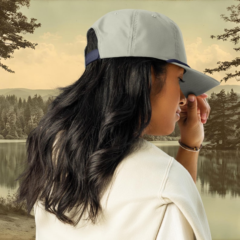 A grey baseball cap with a blue rope and a blue, ochre, and white embroidered smallmouth bass fish on the front.