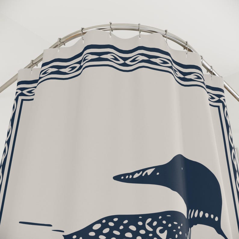 A white shower curtain featuring a navy blue illustration of a loon swimming on water. The loon is detailed with white spots and a black head. The curtain has a navy blue border with a decorative pattern, and is hanging in a rustic bathroom.