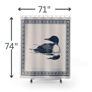 A white shower curtain featuring a navy blue illustration of a loon swimming on water. The loon is detailed with white spots and a black head. The curtain has a navy blue border with a decorative pattern.