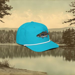 A sky blue baseball cap with a white rope and a blue, ochre, and white embroidered smallmouth bass fish on the front.