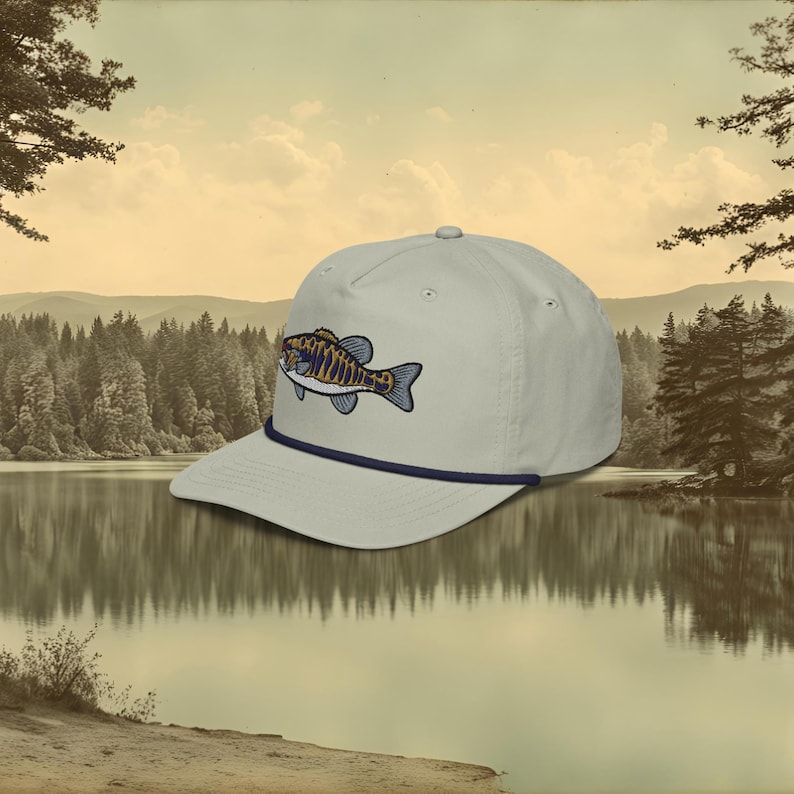 A grey baseball cap with a blue rope and a blue, ochre, and white embroidered smallmouth bass fish on the front.