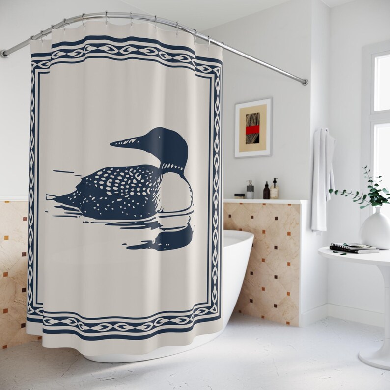 A white shower curtain featuring a navy blue illustration of a loon swimming on water. The loon is detailed with white spots and a black head. The curtain has a navy blue border with a decorative pattern, and is hanging in a rustic bathroom.