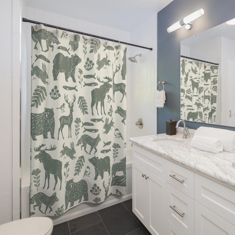 A shower curtain with a repeating pattern of forest animals in dark green on a cream background. The woodland design includes bears, deer, rabbits, foxes, birds, fish, and plants. The curtain has a whimsical log cabin aesthetic.