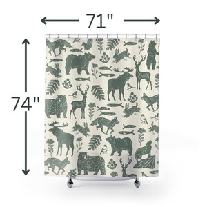 A shower curtain with a repeating pattern of forest animals in dark green on a cream background. The woodland design includes bears, deer, rabbits, foxes, birds, fish, and plants. The curtain has a whimsical log cabin aesthetic.