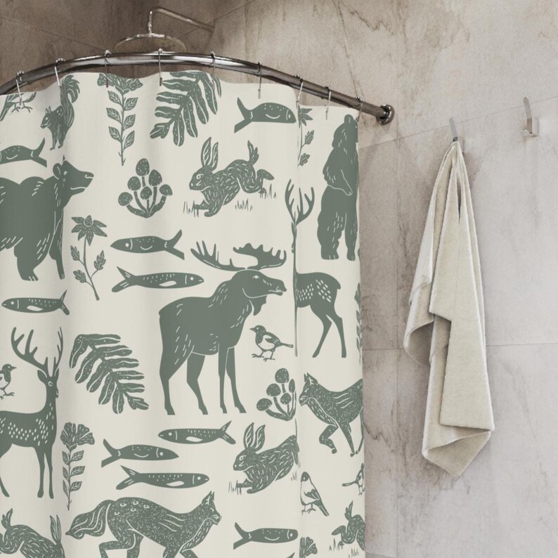 A shower curtain with a repeating pattern of forest animals in dark green on a cream background. The woodland design includes bears, deer, rabbits, foxes, birds, fish, and plants. The curtain has a whimsical log cabin aesthetic.
