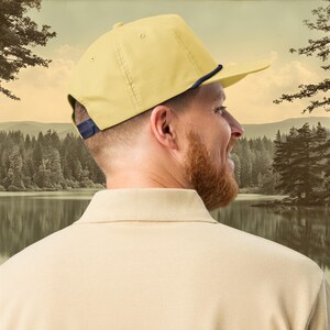 A banana yellow baseball cap with a blue rope and a blue, ochre, and white embroidered smallmouth bass fish on the front.