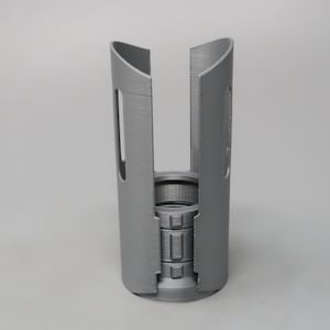 May include: A gray, 3D-printed object with a cylindrical design. The object has a central, detailed core and two curved, vertical panels that partially enclose it. The panels have rectangular cutouts. The object is made of plastic.