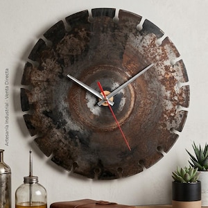 Puede incluir: Un reloj de pared circular fabricado con una hoja de sierra de metal oscuro y desgastado con borde dentado. La esfera presenta manecillas plateadas para las horas y los minutos, junto con un segundero fino de color rojo vibrante.