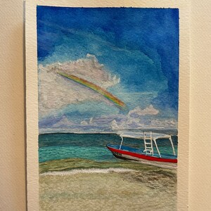 Puede incluir: Pintura a la acuarela de una escena de playa con un arcoíris. Un barco rojo y azul está en el agua, y el cielo es azul con nubes blancas. La palabra "MOON" está en el barco.