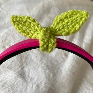 Op de afbeelding: Een limoengroen, gehaakt bladerontwerp bevestigd aan een roze en zwarte headset. De bladeren zijn gedetailleerd met zichtbare steken. De headset is zwart op de oorschelpen.