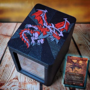 May include: A black rectangular deck box with a glittery finish featuring a red and light purple dragon illustration on the lid. The front has a clear window displaying a trading card. Beside the box lies a Lathliss, Dragon Queen card.