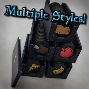 May include: A stack of black plastic holders containing circular tokens with various food icons including a pizza slice, a banana, an apple, and a bone. The text Multiple Styles! is overlaid in blue and white. The holders are arranged in a pyramid.
