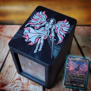 May include: A black rectangular deck box featuring a stained-glass style illustration of an angel with pink and blue wings holding a sword. A Magic: The Gathering trading card titled Giada, Font of Hope is displayed next to the box.