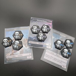 May include: Black and white skeleton-themed game tokens with various power and toughness values, displayed with game cards. The tokens are hexagonal and feature a skeleton design. The cards are labeled "Skeleton" and "Skeleton Pirate".