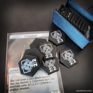 Puede incluir: Fichas de juego negras y grises con temática Cyberman con un valor de 2/2, dispuestas cerca de una carta que dice "Cyberman". Una caja azul contiene fichas adicionales. Las fichas son hexagonales y presentan un diseño Cyberman.
