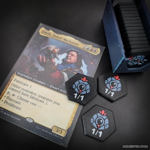 Może przedstawiać: Karta Magic: The Gathering z "Cayth, Famed Mechanist" ze statystykami 3/3, wraz z trzema czarno-niebieskimi żetonami 1/1. Niebieski pojemnik do przechowywania znajduje się w tle. Żetony mają robotyczny design.